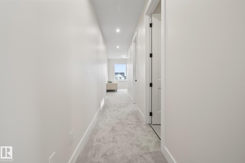 Bright hallway featuring light-toned carpet flooring, recessed lighting, and white walls - 132 Edgewater Circle, Leduc, AB 