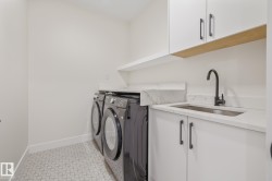 Dedicated laundry space featuring patterned floor tile, stone countertops, a stainless steel sink with a matte black faucet, and white cabinetry with dark hardware - 