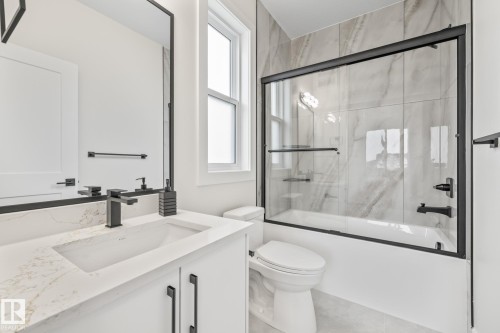 Full bathroom featuring a white vanity with an integrated sink, a dark-framed mirror, and a bathtub with a sliding glass door and tile surround - 132 Edgewater Circle, Leduc, AB 