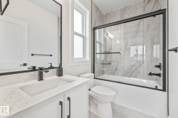 Full bathroom featuring a white vanity with an integrated sink, a dark-framed mirror, and a bathtub with a sliding glass door and tile surround - 