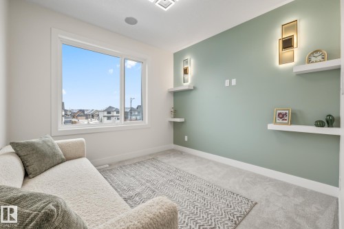 Bright room featuring a large picture window, soft gray carpeting, and a contrasting accent wall with built-in floating shelves and integrated sconce lighting - 132 Edgewater Circle, Leduc, AB 