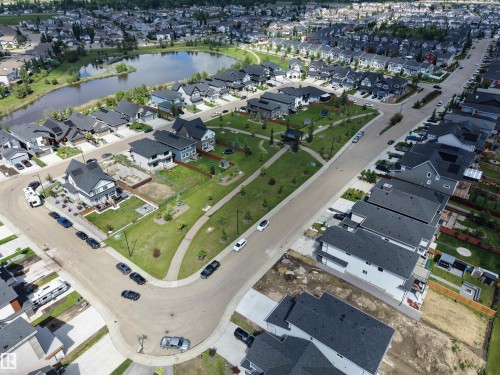 Aerial perspective showcasing a residential neighborhood with numerous detached homes, a central park area, and a reflective pond - 132 Edgewater Circle, Leduc, AB 