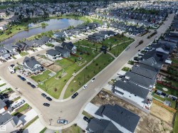 Aerial perspective showcasing a residential neighborhood with numerous detached homes, a central park area, and a reflective pond - 