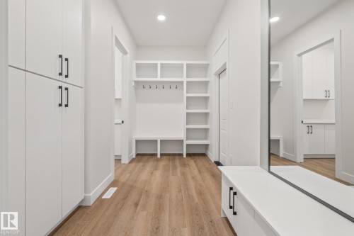Entryway featuring wood-finish flooring, white built-in cabinetry with black hardware, a built-in bench with open shelving, and a full-length mirror - 132 Edgewater Circle, Leduc, AB 
