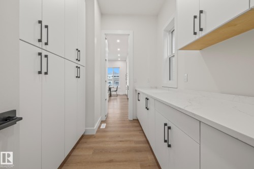 Expansive pantry featuring extensive white cabinetry with matte black hardware, light wood-finish flooring, and white countertops - 132 Edgewater Circle, Leduc, AB 