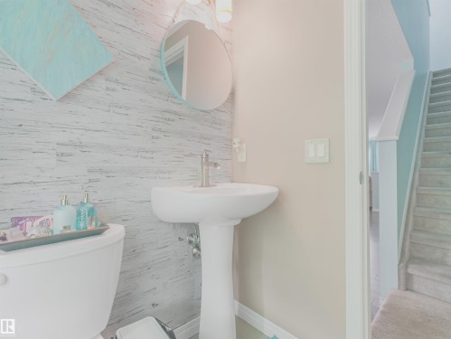 Pedestal sink with a brushed nickel faucet, a round mirror, and a wood-finish accent wall - 44 1140 Chappelle Boulevard, Edmonton, AB 