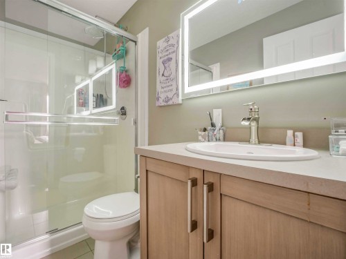 Bathroom featuring a light wood-finish vanity with dual cabinet doors and brushed nickel hardware, an oval undermount sink, and a chrome faucet - 44 1140 Chappelle Boulevard, Edmonton, AB 