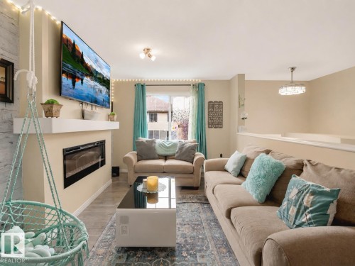Living area featuring wood-finish flooring, an electric fireplace with a white mantel, and a wall-mounted television - 44 1140 Chappelle Boulevard, Edmonton, AB 