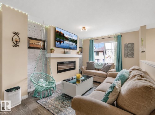 Living area featuring wood-finish flooring, a wall-mounted electric fireplace, and a light-colored accent wall - 44 1140 Chappelle Boulevard, Edmonton, AB 