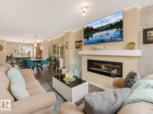 Living room featuring a built-in linear fireplace with a white floating mantle, wood-finish flooring, and a neutral wall palette - 44 1140 Chappelle Boulevard, Edmonton, AB 