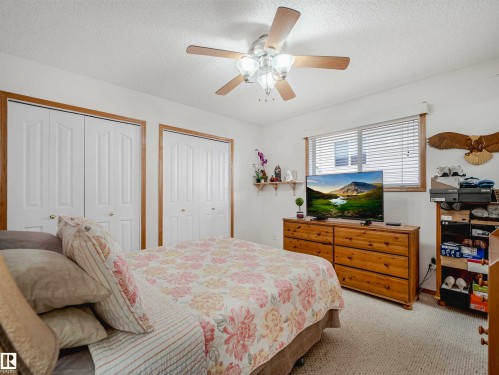 Bedroom featuring neutral wall paint, carpet flooring, a ceiling fan with light fixture, two bi-fold closet doors with wood trim, and a window with blinds - 13825 128A Avenue, Edmonton, AB - Indoor Photo Showing Bedroom