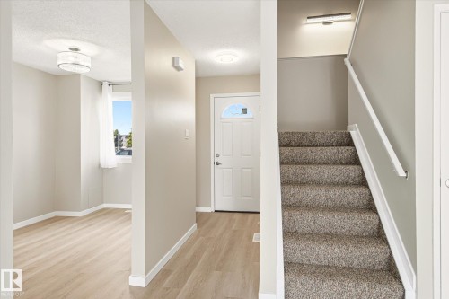 Entryway featuring light wood-finish flooring, a white front door with a decorative glass insert, and a carpeted staircase with a white handrail - 186 Cornell Crest, Edmonton, AB 