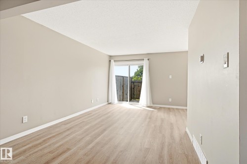 Spacious room featuring light wood-finish flooring, neutral wall tones, and a sliding glass door leading to an outdoor area - 186 Cornell Crest, Edmonton, AB 