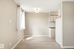 Open-concept living space featuring wood-finish flooring, a contemporary ceiling light fixture, and a window with sheer white curtains - 
