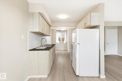 Galley kitchen featuring light wood-finish cabinetry, dark countertops, a white subway tile backsplash, and stainless steel sink - 186 Cornell Crest, Edmonton, AB 