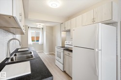 Kitchen featuring light wood-finish cabinetry, dark countertops, and a white appliance suite - 