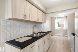 Kitchen featuring light wood-finish cabinetry with silver hardware, dark countertops, and a stainless steel double sink - 