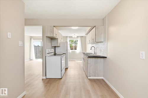 Galley kitchen featuring light wood-finish cabinetry, dark countertops, a white appliance package, and a tile backsplash - 186 Cornell Crest, Edmonton, AB 