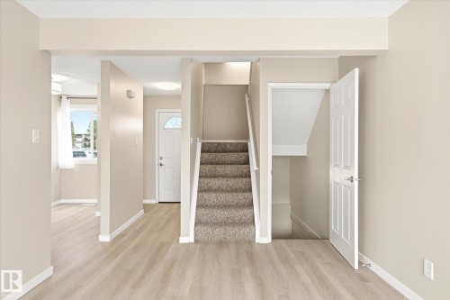 Foyer featuring light wood-finish flooring, a carpeted staircase with white railing, and a white paneled door with hardware - 186 Cornell Crest, Edmonton, AB 