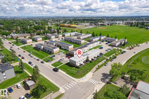 Aerial view showcasing the property within a residential development, featuring multiple residential buildings with solar panels, surrounding green spaces, and a nearby sports field - 186 Cornell Crest, Edmonton, AB 