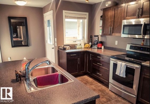 Kitchen featuring dark wood cabinetry, stainless steel appliances, a double basin sink with a pull-down faucet, and durable countertop surfaces - 12246 103 Street, Edmonton, AB - Indoor Photo Showing Kitchen With Double Sink