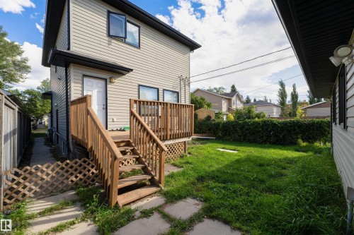 Rear exterior featuring a wooden deck with railing and stairs, light-colored siding, black window trim, and a green lawn - 12246 103 Street, Edmonton, AB - Outdoor