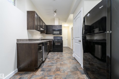 Kitchen featuring dark wood-finish cabinetry, black appliances, a tile backsplash, and multi-toned floor tiling - 12246 103 Street, Edmonton, AB - Indoor Photo Showing Kitchen