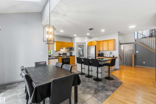 Open-concept kitchen and dining area featuring light wood cabinetry, stainless steel appliances, dark countertops, and a kitchen island with seating - 3061 Spence Wynd, Edmonton, AB 