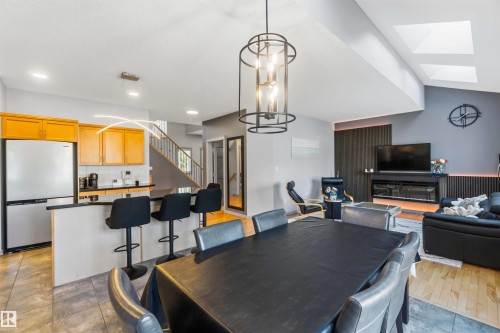 Open-concept living area featuring a kitchen island with bar seating, skylights, a modern chandelier, a built-in electric fireplace, and wood-finish flooring - 3061 Spence Wynd, Edmonton, AB 
