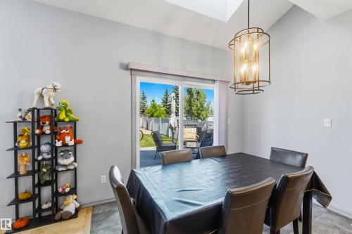 Dining area featuring a modern cylindrical pendant light, vaulted ceiling with a skylight, and sliding glass doors opening to a rear deck - 3061 Spence Wynd, Edmonton, AB 