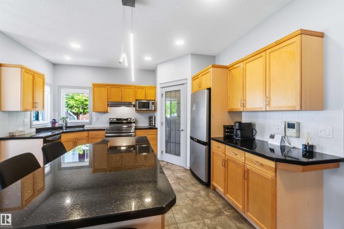 Kitchen featuring a large island with a dark, speckled countertop, light wood cabinetry, stainless steel appliances, and tile flooring - 3061 Spence Wynd, Edmonton, AB 