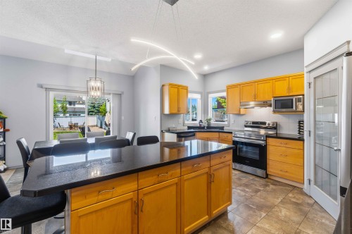 Kitchen featuring light wood cabinetry, dark countertops, and stainless steel appliances - 3061 Spence Wynd, Edmonton, AB 