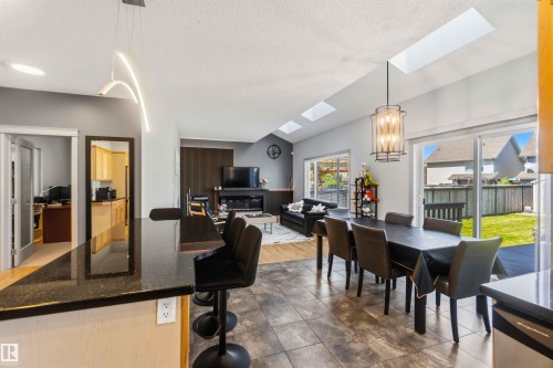 Open-concept living space featuring vaulted ceilings with multiple skylights, a kitchen island with a dark granite countertop, large format tile flooring, and a sliding glass door opening to the backyard - 3061 Spence Wynd, Edmonton, AB 