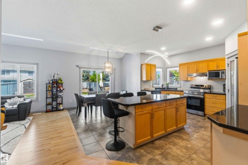 Open-concept living space featuring a central kitchen island with seating, stainless steel appliances, and wood-finish cabinetry - 3061 Spence Wynd, Edmonton, AB 