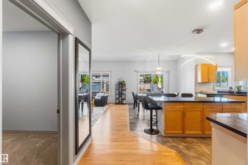 Open-concept kitchen and dining area featuring light wood cabinetry, dark countertops, and a central island with bar seating - 3061 Spence Wynd, Edmonton, AB 