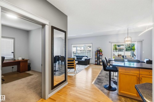 Open concept living area featuring wood-finish flooring, a kitchen island with dark countertops, and a dining space with a contemporary chandelier - 3061 Spence Wynd, Edmonton, AB 