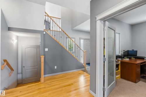 Foyer featuring wood-finish flooring, a staircase with wood handrails and wrought iron balusters, and a wall sconce illumination - 3061 Spence Wynd, Edmonton, AB 