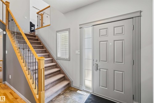 Foyer featuring a paneled front door with decorative side light, wood-finish flooring, a staircase with wood handrails and wrought iron balusters, and a neutral wall color - 3061 Spence Wynd, Edmonton, AB 