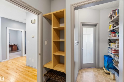 Entryway featuring light wood-finish flooring, a built-in shelving unit, and a pantry with frosted glass door and extensive shelving - 3061 Spence Wynd, Edmonton, AB 