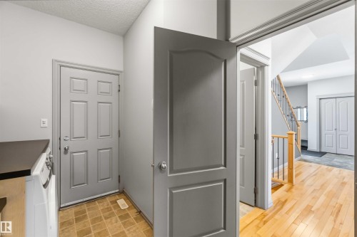 Entryway featuring a paneled door, wood-finish flooring, and staircase with wooden handrail and metal spindles - 3061 Spence Wynd, Edmonton, AB 