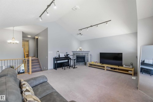 Spacious living area featuring a corner fireplace with a tiled surround and mantel, vaulted ceilings, track lighting, and soft carpet flooring - 3061 Spence Wynd, Edmonton, AB 
