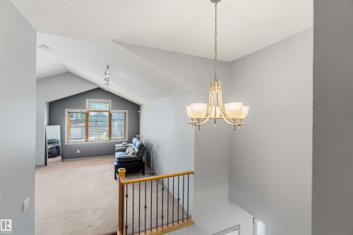 Vaulted ceiling living area featuring a decorative chandelier, expansive window arrangement, and plush carpet flooring - 3061 Spence Wynd, Edmonton, AB 