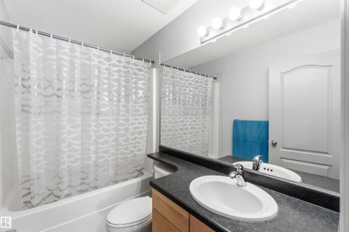 Bathroom featuring a white bathtub, toilet, and vanity with an oval undermount sink, dark countertop, and wood-finish cabinetry - 3061 Spence Wynd, Edmonton, AB 