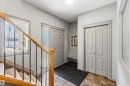 Entryway featuring wood-finish flooring, a staircase with wood newel posts and metal balusters, a paneled entry door with frosted glass side light, a built-in bench, and a pair of paneled bifold doors - 3061 Spence Wynd, Edmonton, AB 