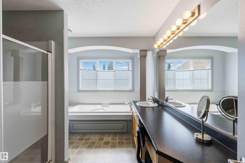 Bathroom featuring a dual vanity with a dark countertop and two integrated sinks, a large mirror, and a linear vanity light fixture - 3061 Spence Wynd, Edmonton, AB 