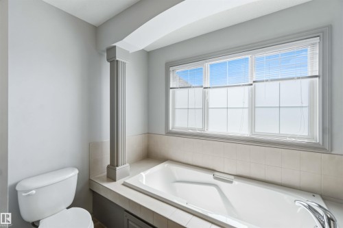 Soaking tub with tiled surround and integrated shelving beneath a large three-pane window - 3061 Spence Wynd, Edmonton, AB 
