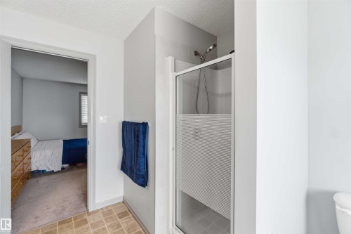 Bathroom featuring a glass-enclosed shower with frosted privacy paneling, chrome fixtures, and neutral-toned wall tiling - 3061 Spence Wynd, Edmonton, AB 