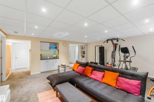 Spacious recreational room featuring recessed lighting, plush carpeting, a built-in wet bar with a tiled backsplash, and a dedicated exercise area - 3061 Spence Wynd, Edmonton, AB 
