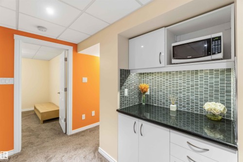 Kitchenette featuring a black countertop, glass mosaic tile backsplash, white cabinetry, and an integrated microwave - 3061 Spence Wynd, Edmonton, AB 