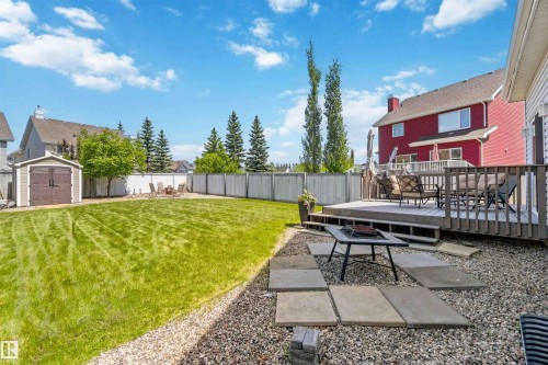 Expansive backyard featuring a large wooden deck, gravel patio with stepping stones, manicured lawn, storage shed, and perimeter fencing - 3061 Spence Wynd, Edmonton, AB 